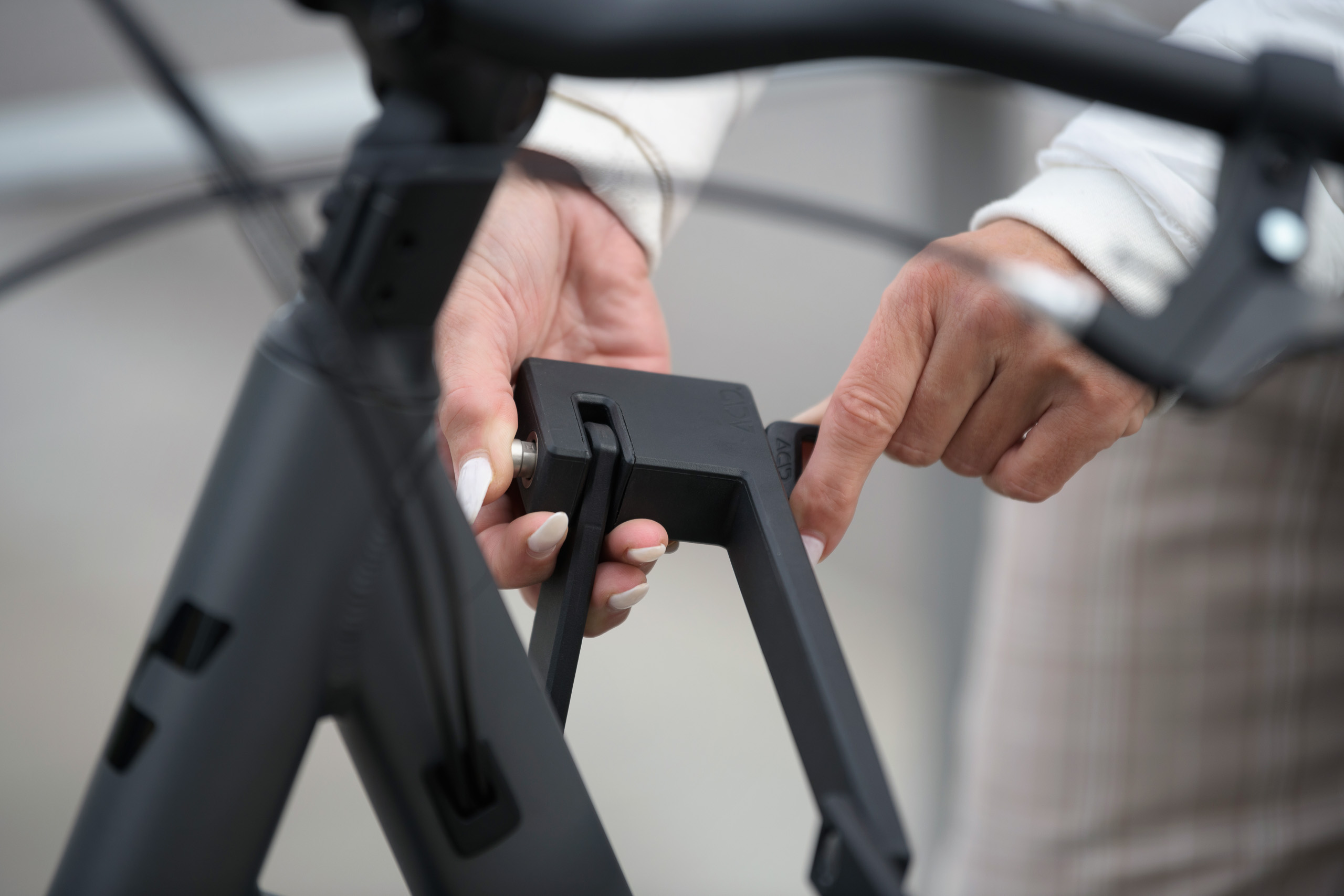 Nahaufnahme der Hände einer Person, die ein CUBE-Fahrrad mit einem schwarzen Schloss abschließt, wobei der am Fahrradrahmen befestigte Schließmechanismus im Mittelpunkt steht – aufgenommen vor dem CUBE Store Deggendorf.