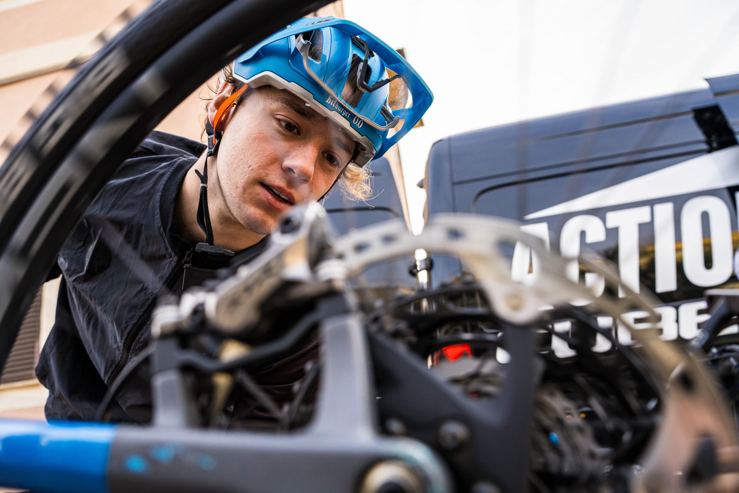 Eine Person mit blauem Helm nimmt die Schaltung und Komponenten eines Fahrrads genau unter die Lupe. Im Hintergrund ist ein schwarzer Lieferwagen zu sehen, auf dem teilweise ein weißer Text des CUBE Store Deggendorf zu sehen ist.